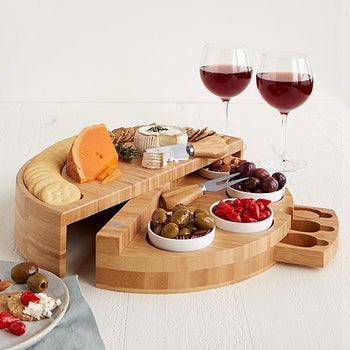 Cheese plate opened up to reveal swivel compartment with various snacks and toppings, and the hidden drawer opened to reveal cheese knives