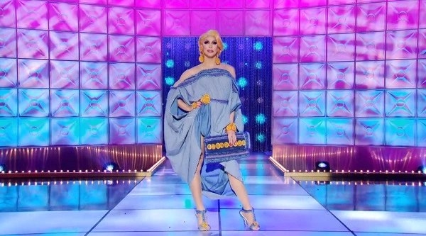 Drag queen Brooke Lynn Hytes wearing a denim caftan dress with matching purse and orange accessories