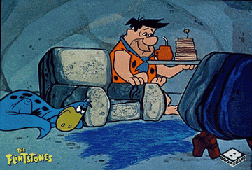 Fred Flintstone turns on a TV while sitting in a chair with a handful of snacks during an episode of &quot;The Flintstones.&quot;