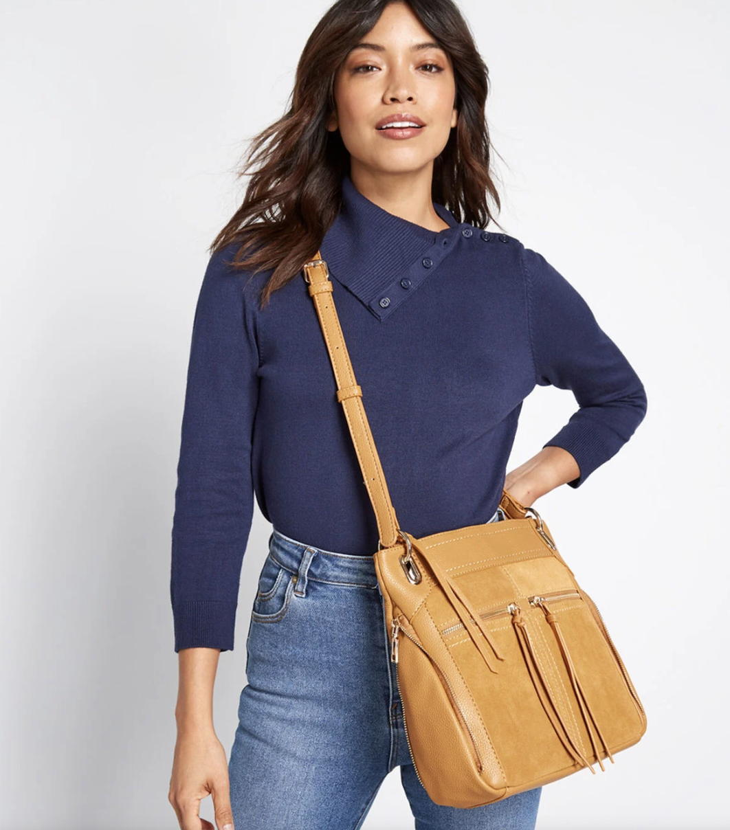 Model with a yellow cross body messenger bag with tasseled zippered front pockets 