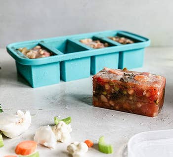 The five-compartment teal container that looks like a large ice cube tray, with a perfectly rectangular block of frozen soup next to it 