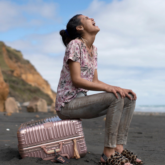 A teen girl sits on a suitcase on the beach and cries