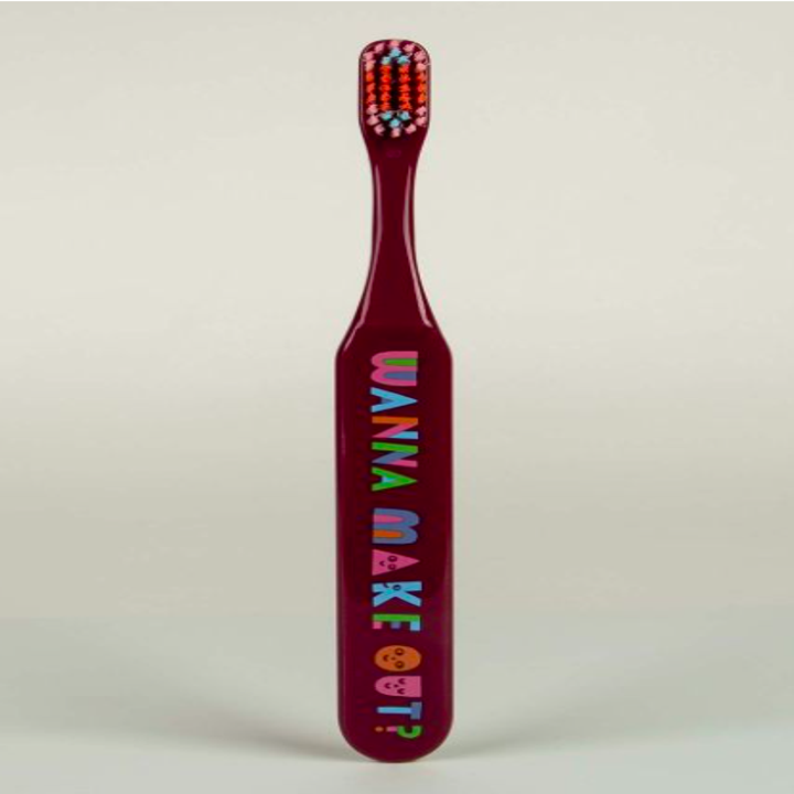Burgundy toothbrush with the text "wanna make out?" on the handle in colorful block letters