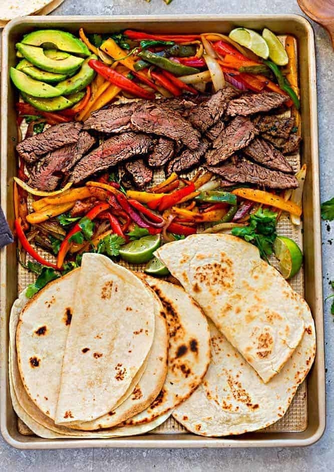 A sheet pan with roasted veggies, sliced steak, and tortillas.