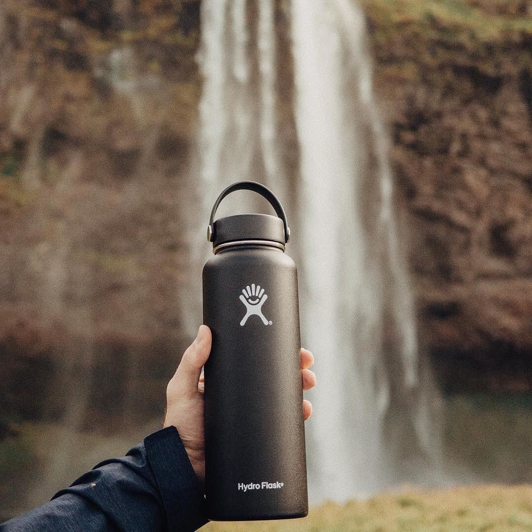 A person holding a Hydro Flask in front of a waterfall