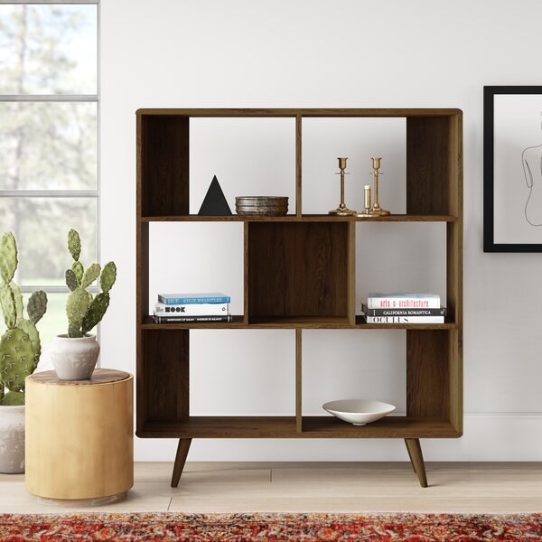 The bookcase, which has four small slanted legs, and a rectangular body with three shelves—two of them are divided into two compartments, while one is divided into three compartments