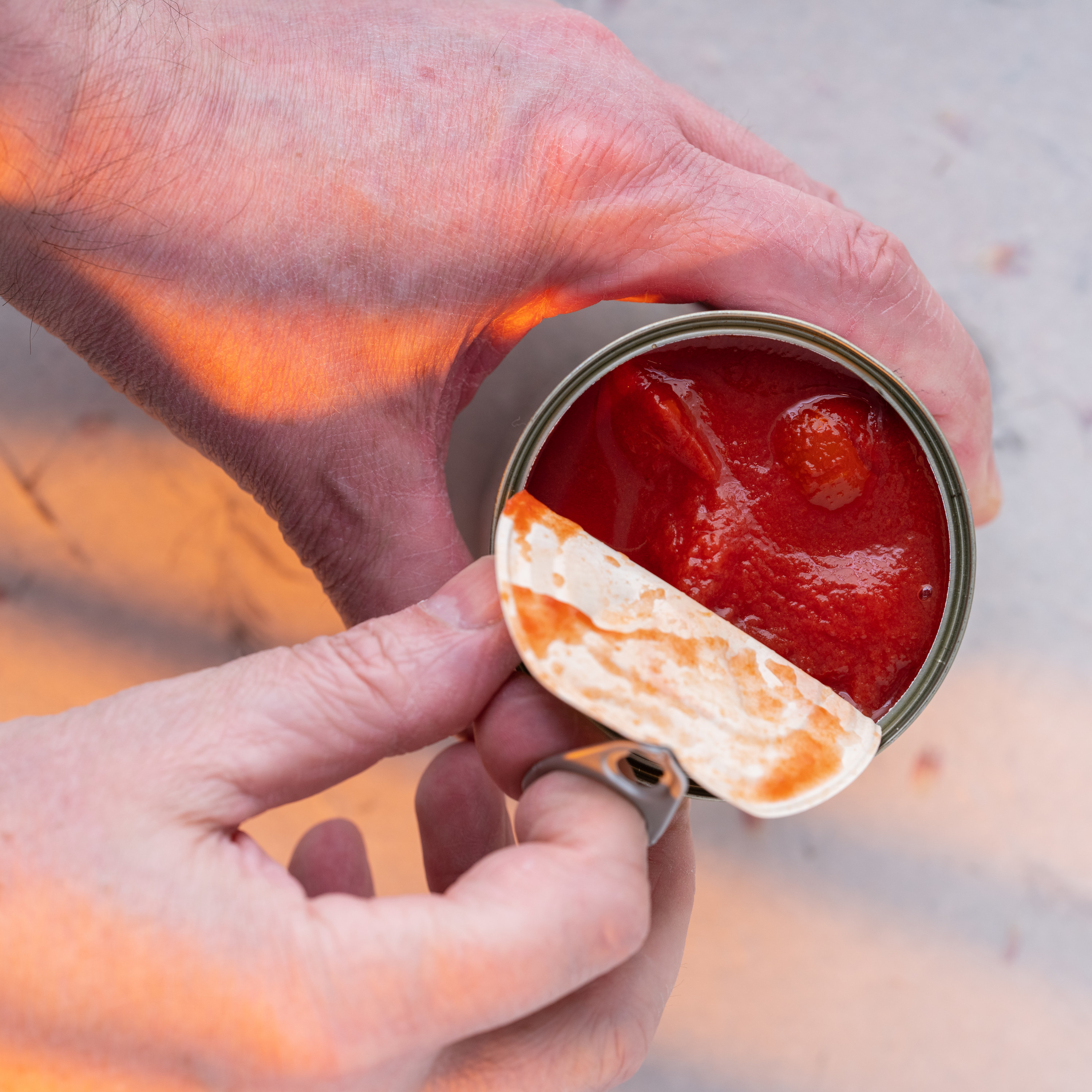 A human hand peels back the lif of canned tomatoes