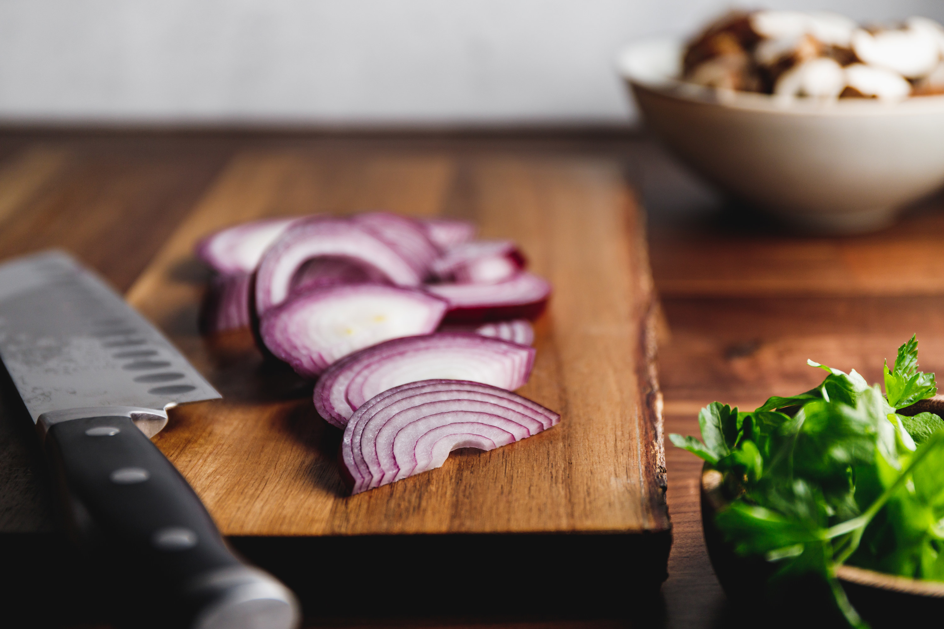 Purple onions chopped on a cutting board next to a knife, mint, and mushrooms