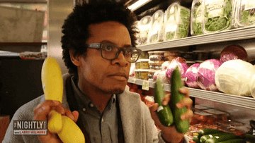 Larry Wilmore shakes squash and zucchini in his hands as if testing them on The Nightly Show with Larry Wilmore