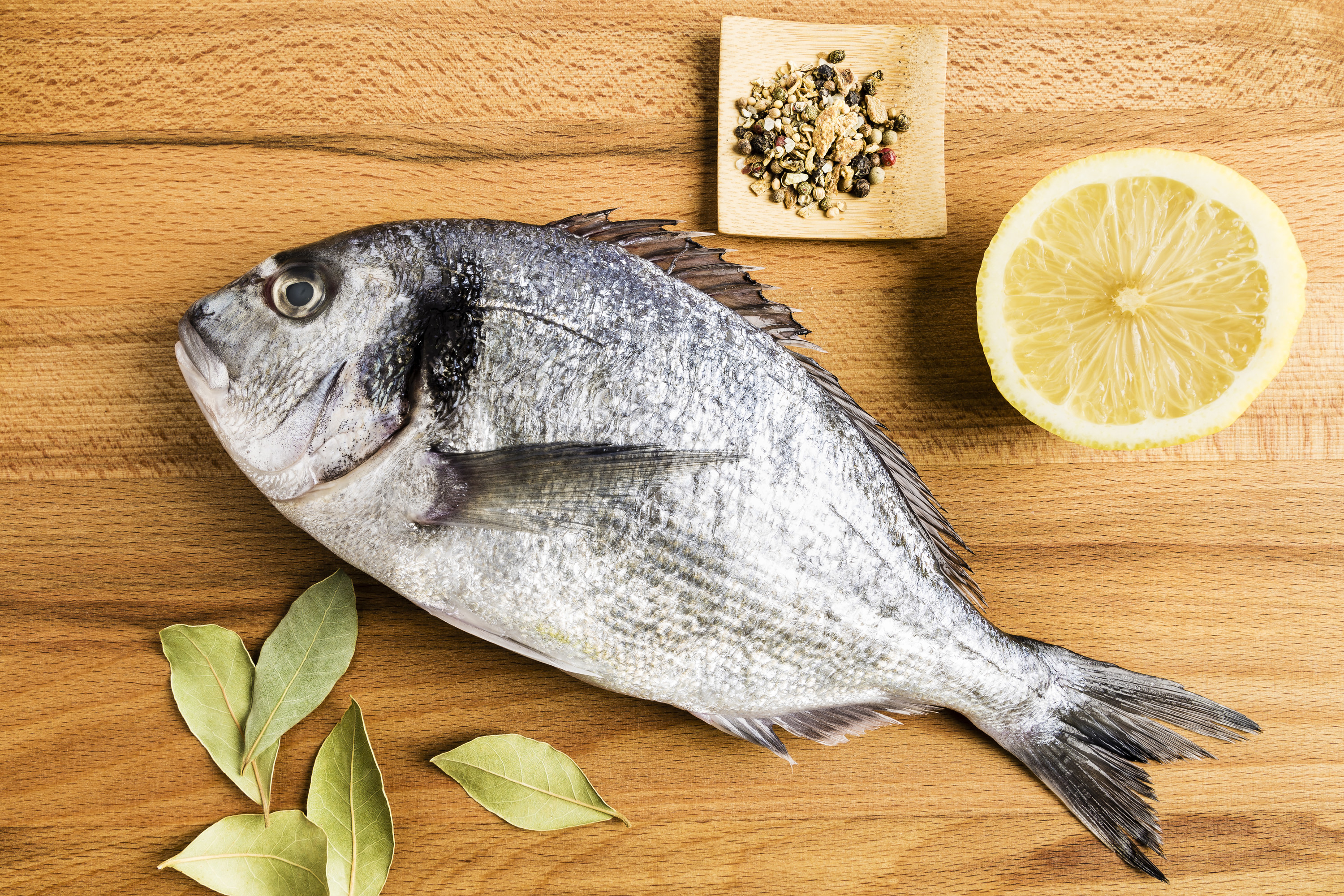 A cooked whole fish lays on its side next to a slice of lemon and some seasoning 