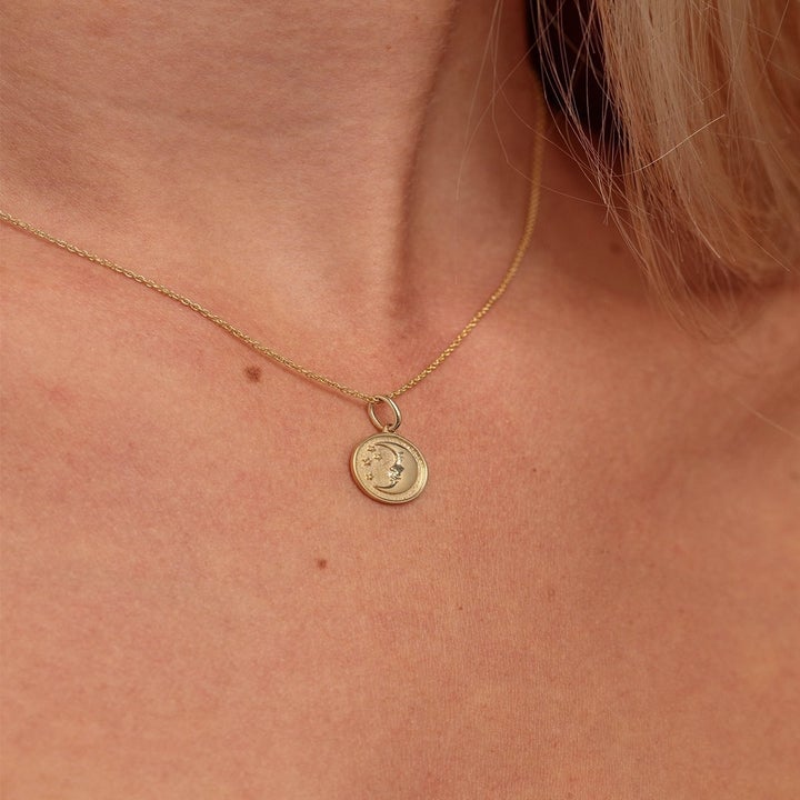 a model wearing a gold necklace with a moon medallion attached to it