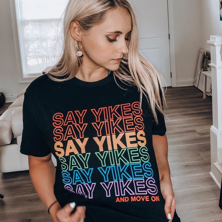 a model in a black tee with "say yikes" in a rainbow pattern