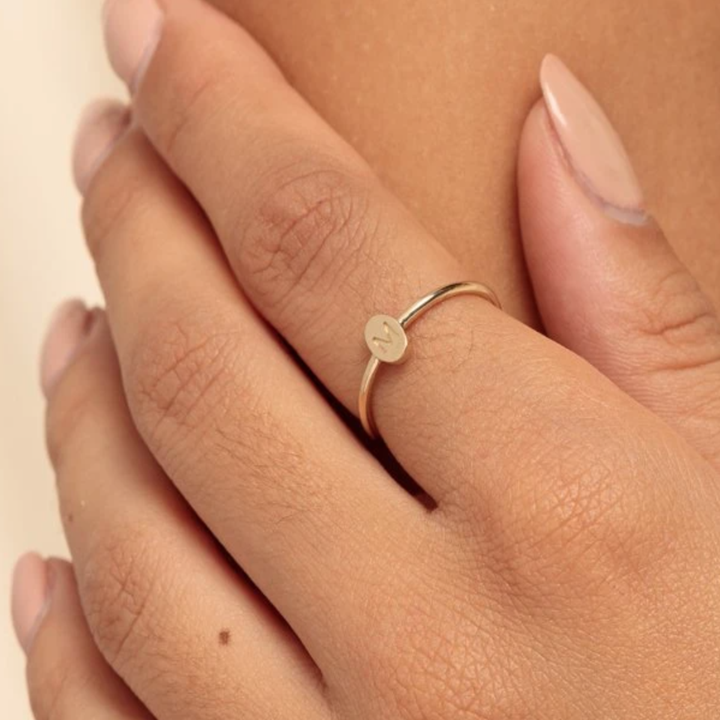 a model wearing a thin ring with a tiny initial circle on it