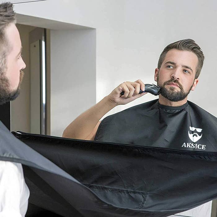 A model trimming their beard with a plastic &quot;bib&quot; that suctions itself to the mirror, catching the hair 