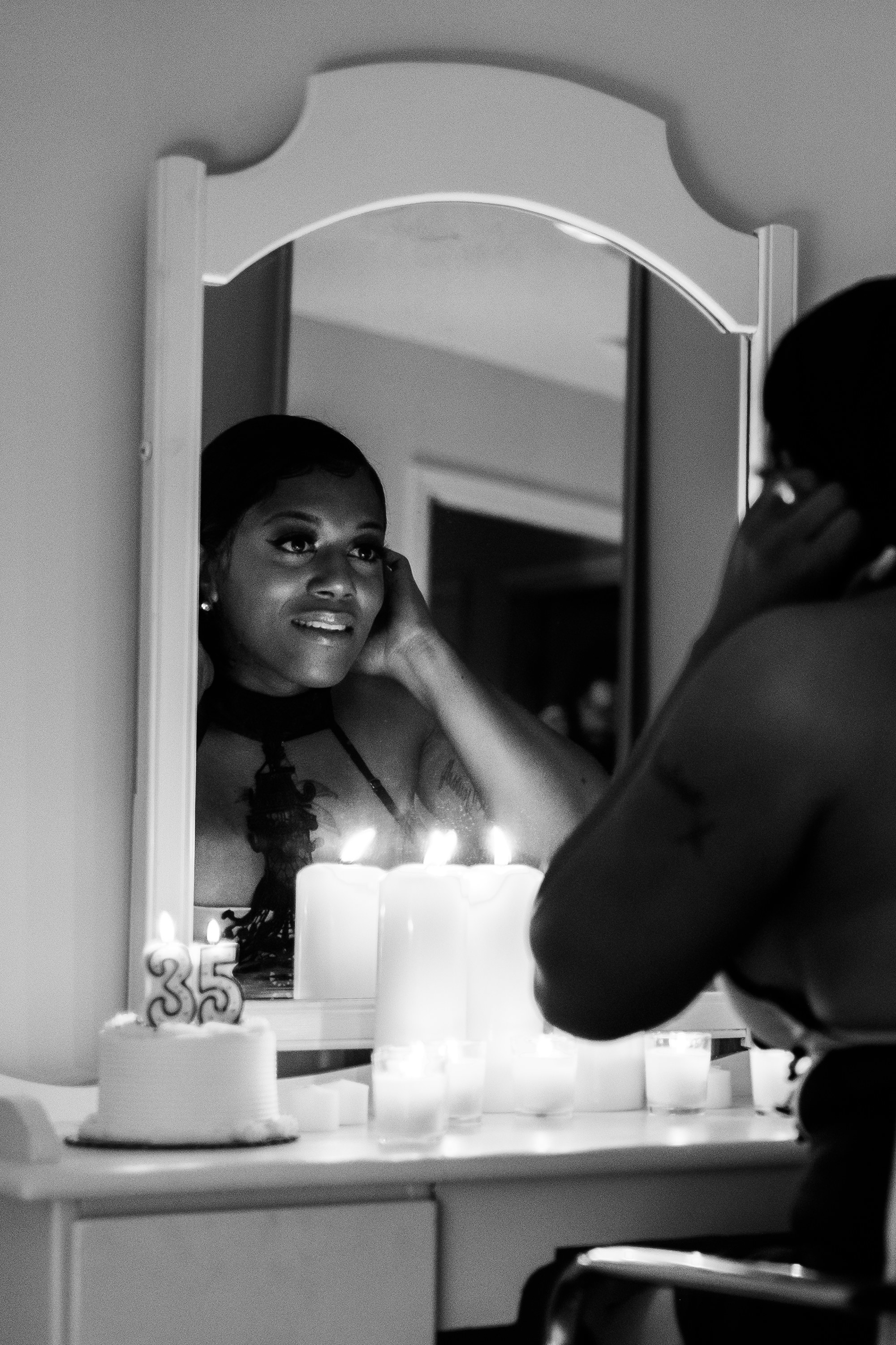 A black trans woman looks into the mirror and smiles candles are nearby