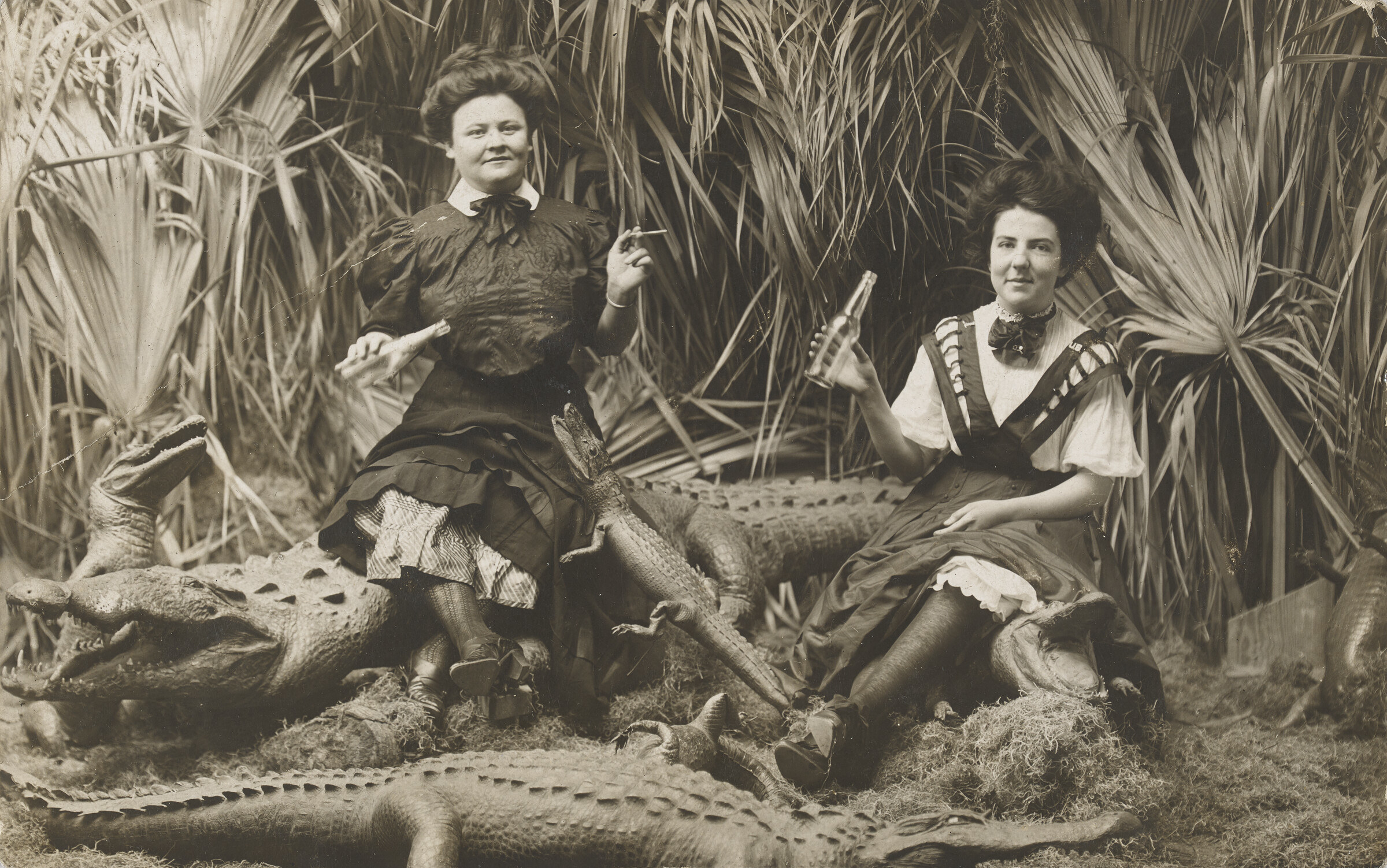 A black-and-white photograph of two women smoking and drinking out of bottles surrounded by fake alligators