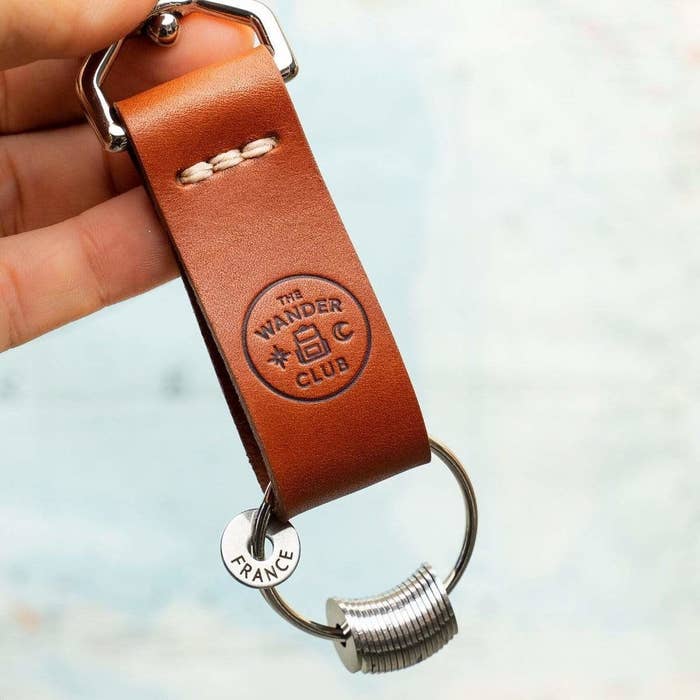 A brown keychain with a keyring holding several engraved tokens; one is engraved to say France