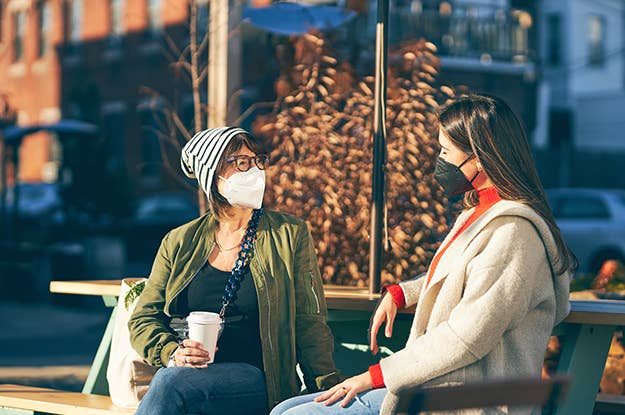Two women sitting on a bench wearing KN95 masks