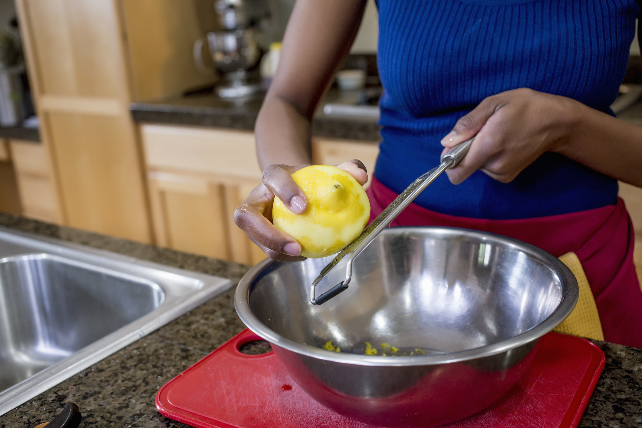 A women zesting a lemon over a bowl in the kitchen