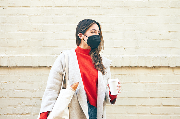 Woman holds coffee while wearing a KN95 mask