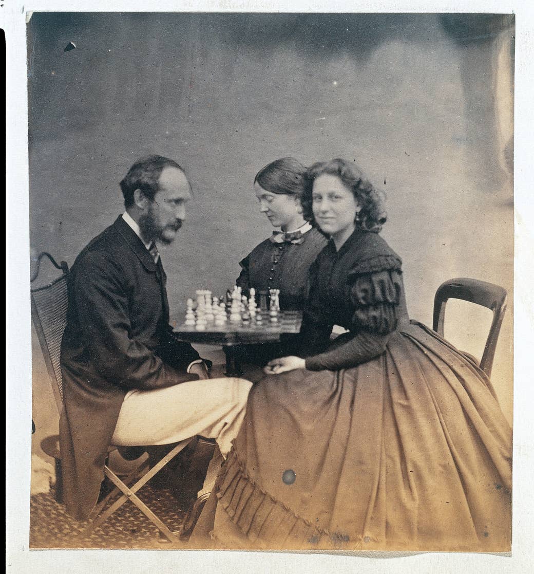 An old photograph of two women sitting across a table and playing chess with a man