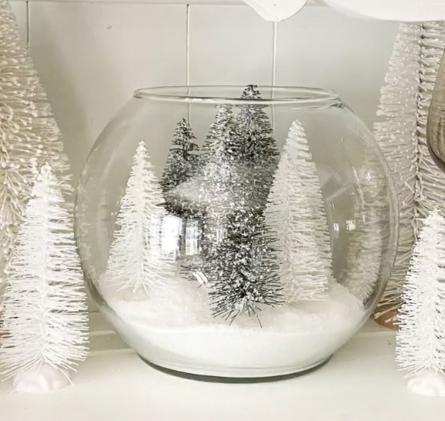 A glass bowl filled with snow and mini trees