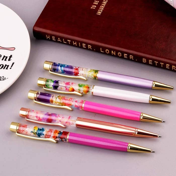 The five gold pens with clear tops filled with small flowers, each with a different color bottom half in shades of pink and purple