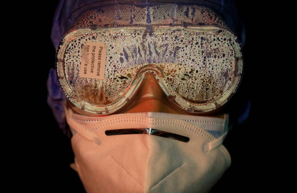 The goggles of a woman wearing two face masks are coated in vapor; a sticker attached to their front reads &quot;Please remove the protective film before use&quot;