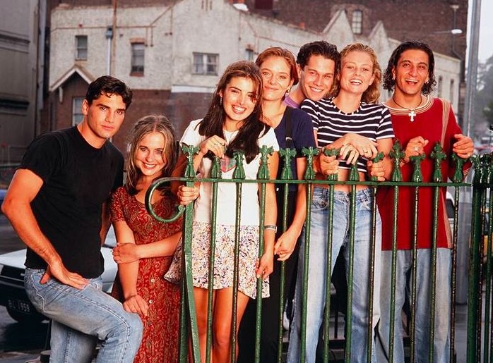 The cast of Heartbreak High pose for a promo photo standing behind a metal fence
