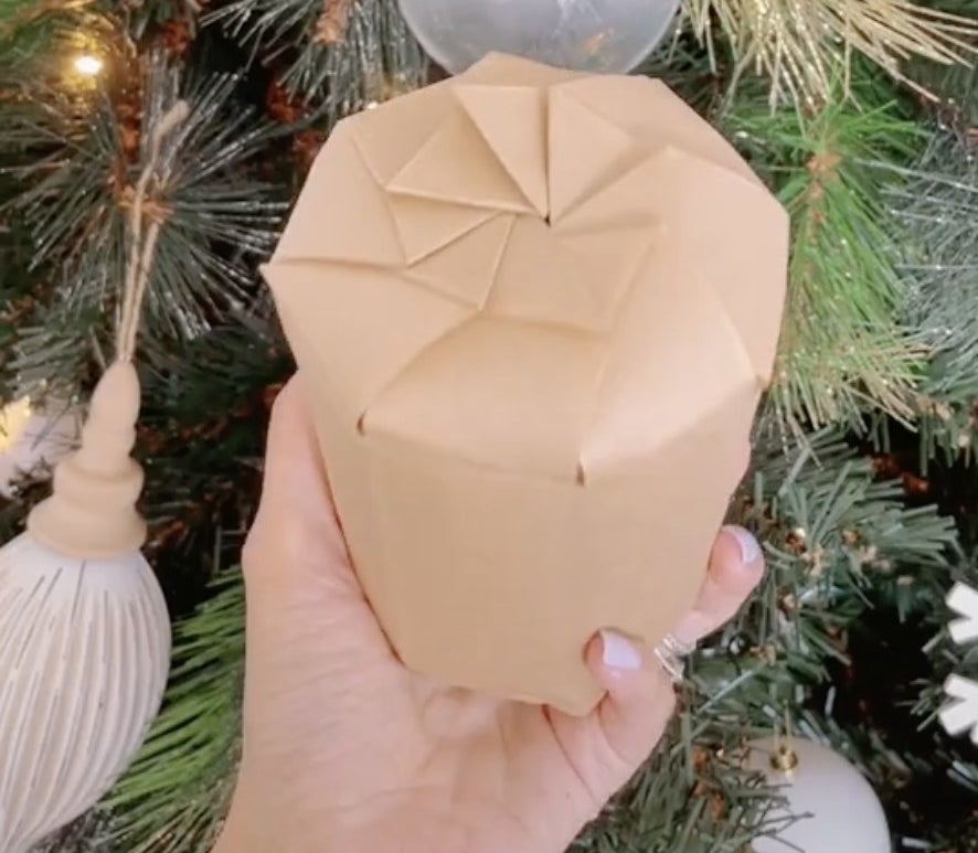A candle wrapped in brown paper with intricate folds on top