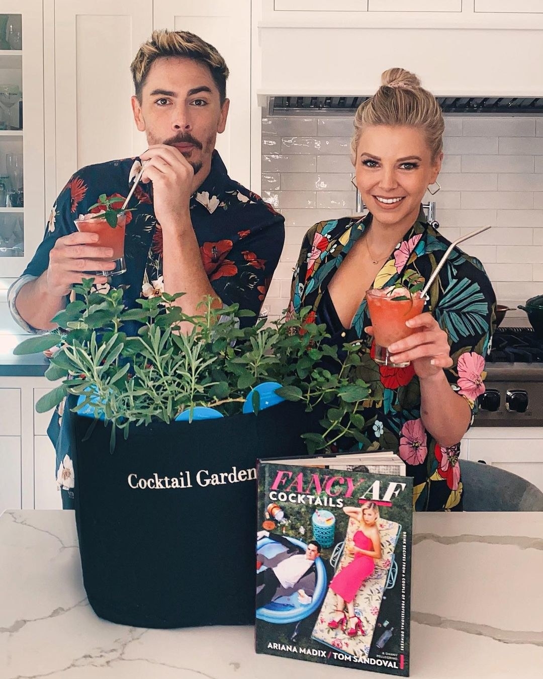 tom and ariana holding drinks with a cocktail garden kit and their book in front of them