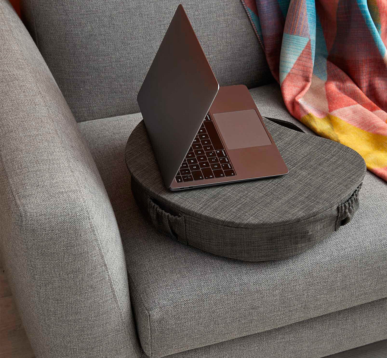 A laptop on the padded laptop table next to a blanket