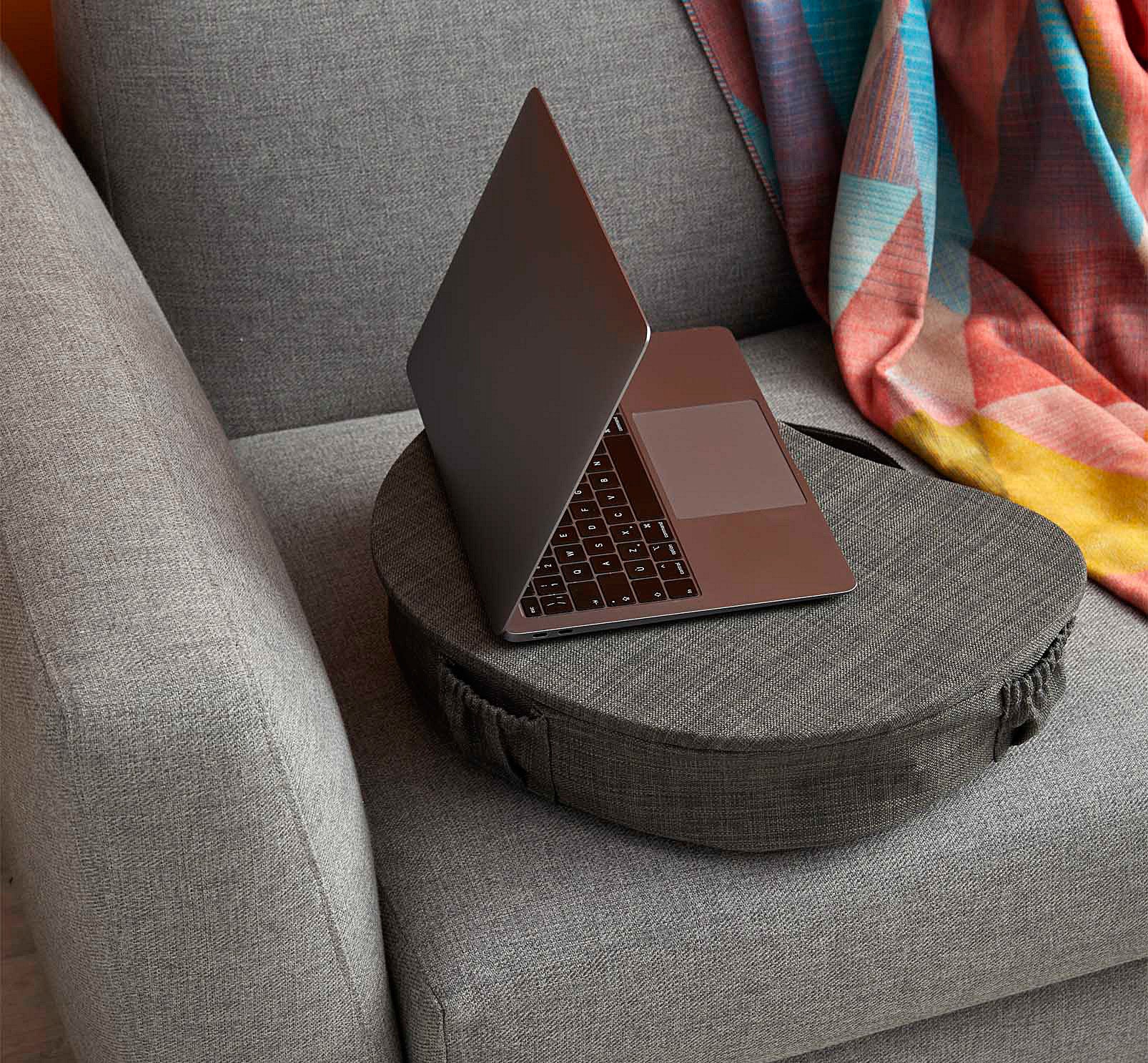 A laptop on the padded laptop table next to a blanket