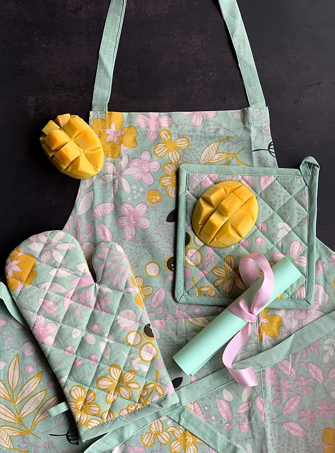 A pastel teal apron with oven mitts and a pot holder that has a yellow and pink floral pattern on it.