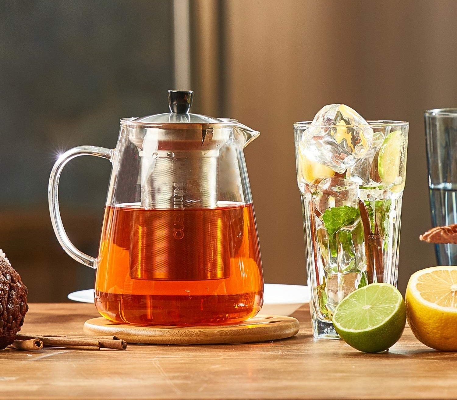 A glass teapot full of tea next to a glass of ice
