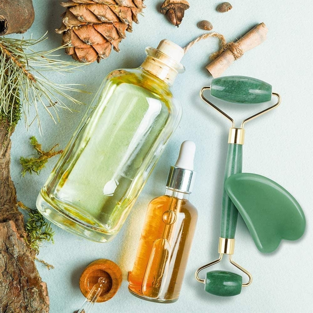 Two bottles of oil beside the double-sided jade facial roller and a jade gua sha tool