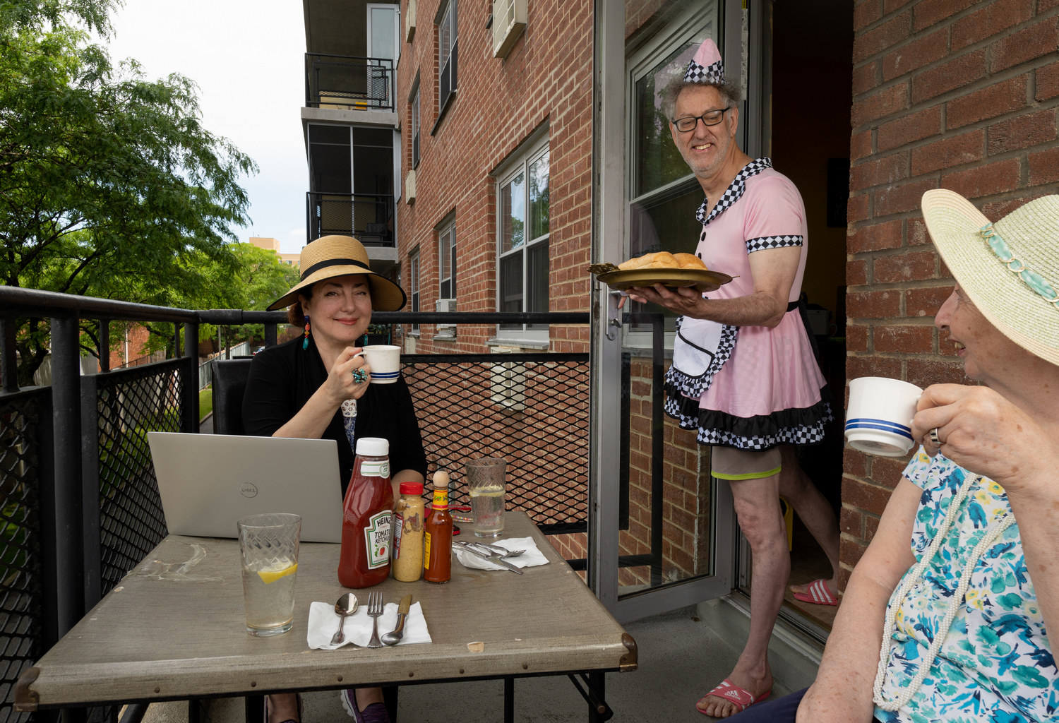 Two women dining on a balcony while a man in a server costume brings them food