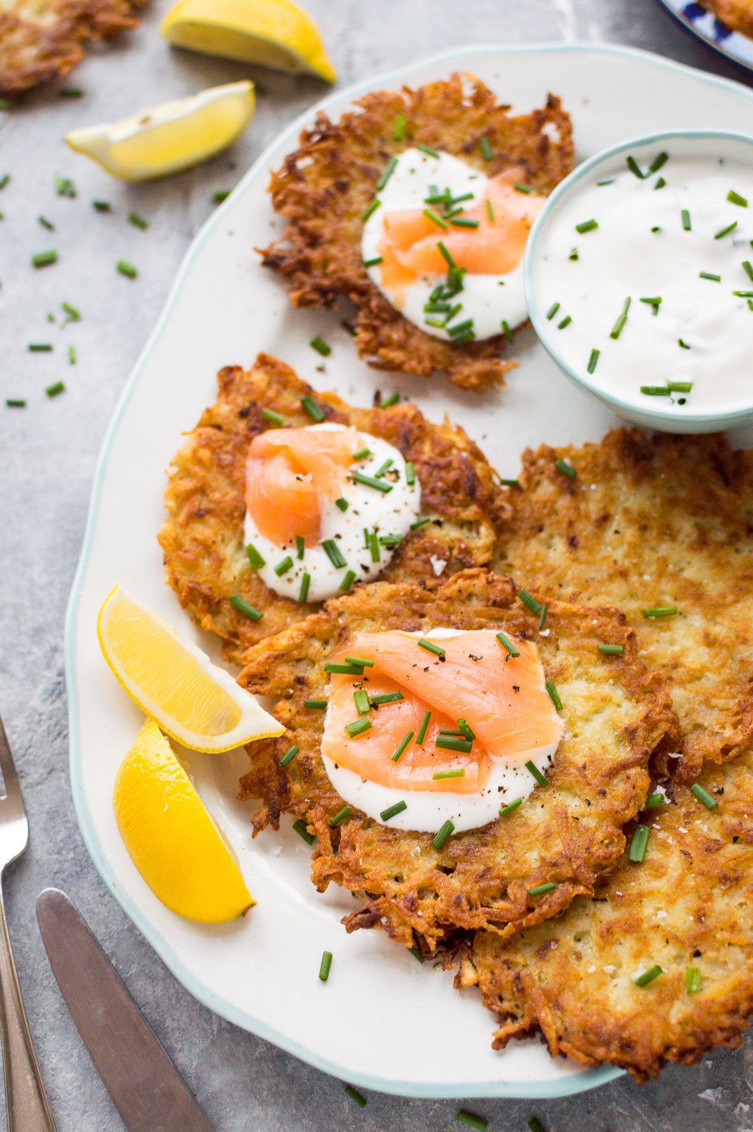 A plate of crispy potato latkes topped with sour cream, smoked salmon, and chives.