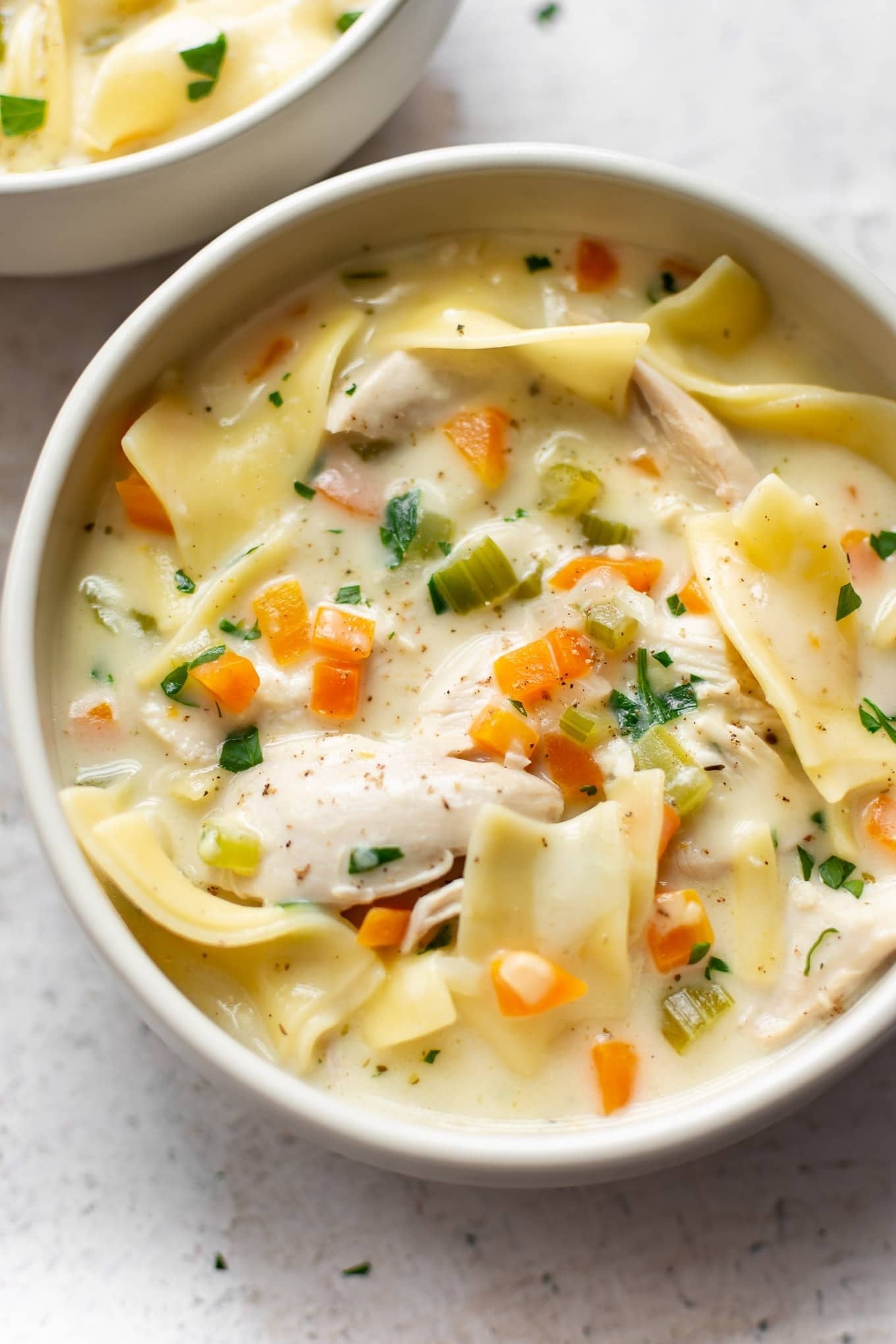 A bowl of creamy chicken noodle soup with carrots, celery, and herbs.