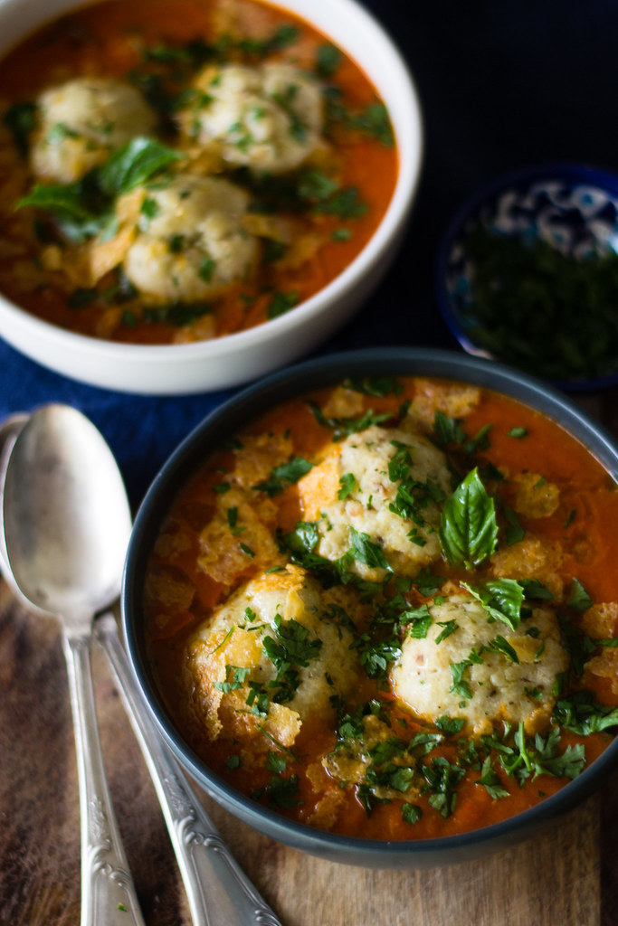 A bowl of tomato-based soup with three fluffy matzo balls topped with fresh herbs.