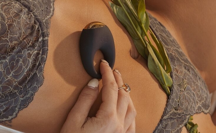 Hand holds black Halo by Bellesa cock ring against model&#x27;s chest