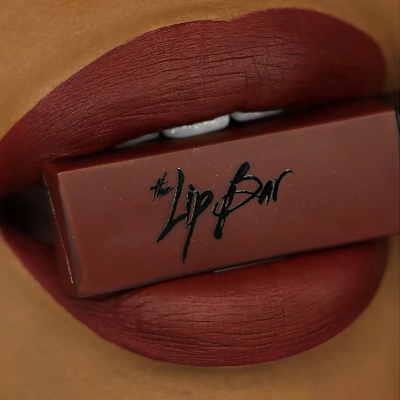 A model wearing The Lip Bar lipstick in the dark red color, &quot;Rebel&quot;