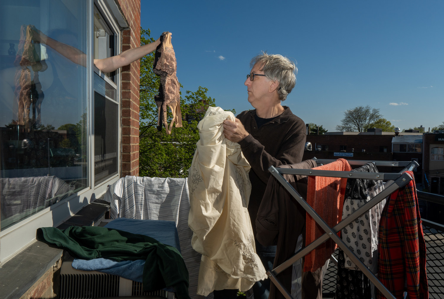 A man drying laundry on the balcony while a woman hands him bras out the window