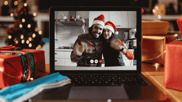 A man and woman wear Santa hats and wave through the computer screen