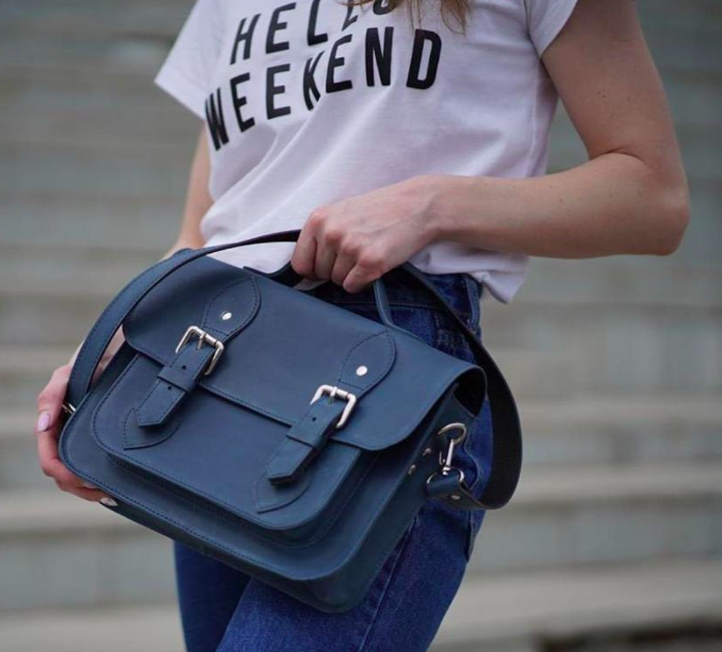 A person holding the satchel against a pair of jeans