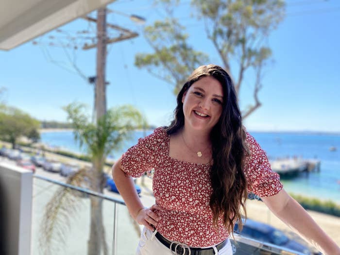 Woman standing on a balcony wearing a red shirt with the ocean in the background