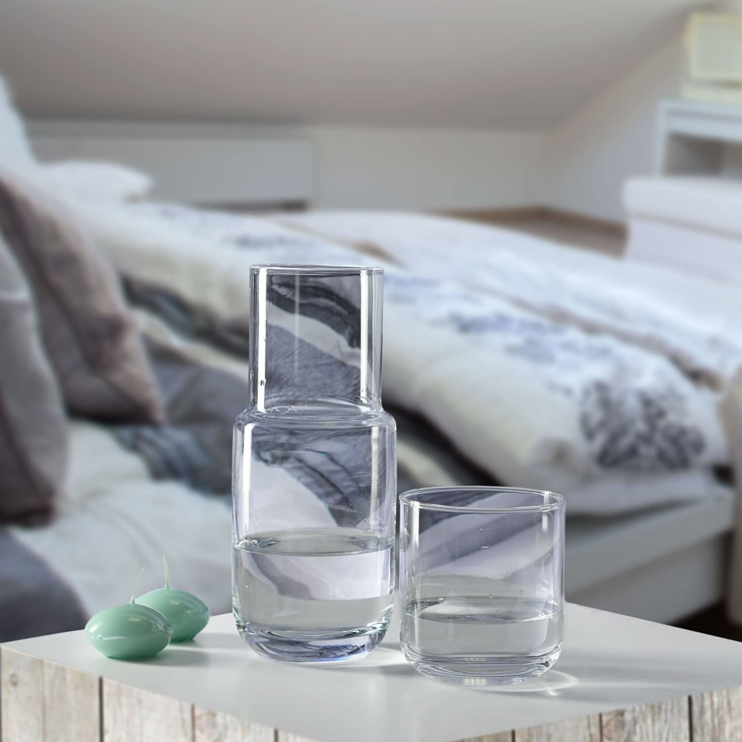 A glass carafe with a matching glass perched on a bedside table