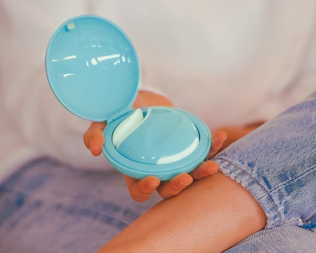 Model holds blue discreet vibrator in matching clamshell-like case