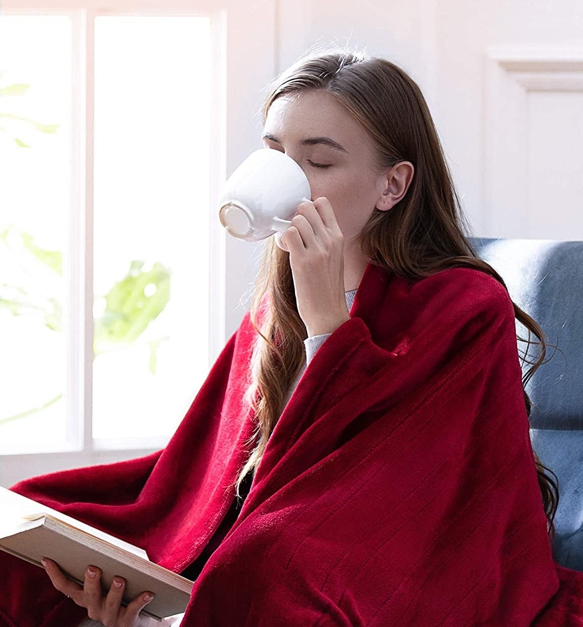 person drinking out of a mug with the blanket wrapped around them