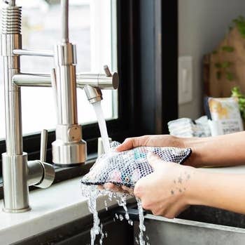 A model rinsing the washable sponge under the sink faucet 